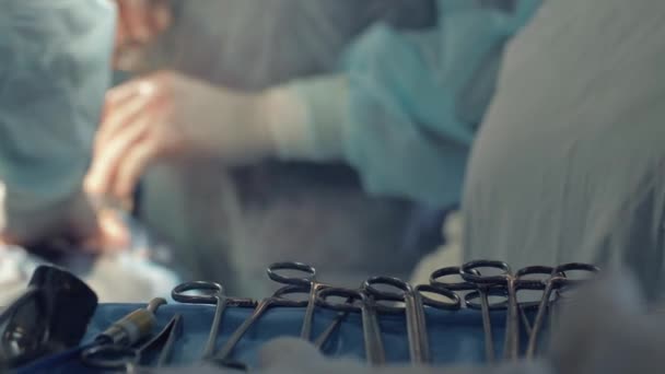 Крупним планом хірургічні інструменти, розмитий фон медсестри, що дає скальпель хірургу, руки медичної команди, що виконує операцію — стокове відео