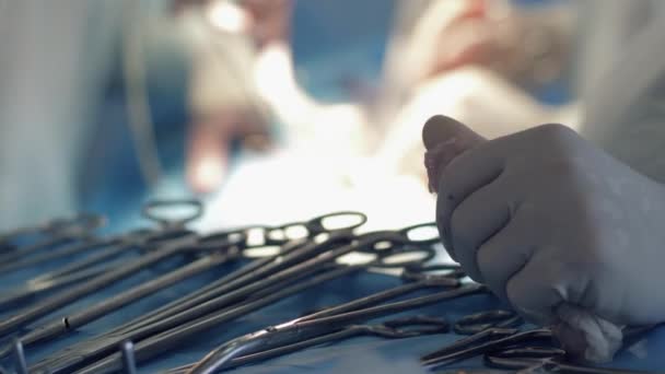 Tratamento cirúrgico, mãos de enfermeira em luvas de sangue perto de ferramentas de cirurgia perto de fundo embaçado de médicos que realizam operação médica — Vídeo de Stock