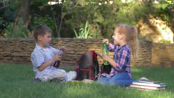 Törstiga barn skruva av locken på flaskorna och drick snabbt juicen under lunchen på skolgården — Stockvideo
