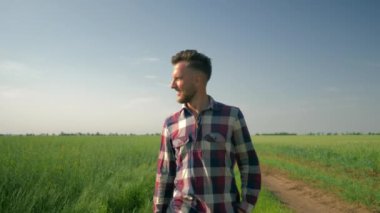 Mutlu çiftçi köy yolunda yürüyor sonra bir cep telefonu çıkarıyor ve yeşil tarla ve mavi gökyüzünün arka planında selfie çekiyor.