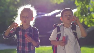 Okul çocukları teneffüste bir kız ve bir oğlan açık havada arka planda bir sürü sabun köpüğü üfler.