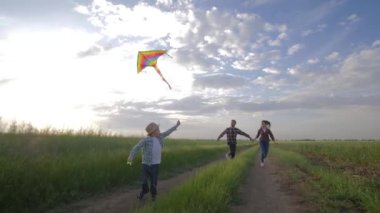 Uçan aile uçurtması, genç anne ve babası olan bir çocuk hafta sonu boyunca doğada gökyüzünün arka planında koşuyor.