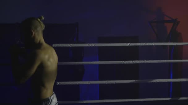 Боксерская подготовка, спортсмен отрабатывает удары в ринге в сумерках перед боем — стоковое видео