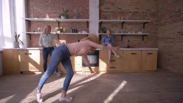 Ευτυχισμένη ευέλικτη κοπέλα κάνει γυμναστική τούμπα μπροστά από τη μαμά και την αδελφή στην κουζίνα στο σπίτι — Αρχείο Βίντεο