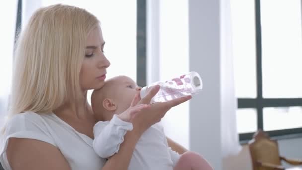 Baby care, young happy mother holds infant girl in arms and gives to drink water from bottle — Stock Video