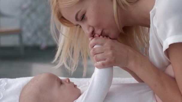 Związek matka i dziecko, rodzic pocałunki małe ręce jej urocza córka dziecka, który leży na zmianę tabeli zbliżenie — Wideo stockowe