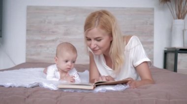 kitap ile sevgi dolu anne evde yatakta yatan bebek kızı masal hikaye anlatıyor