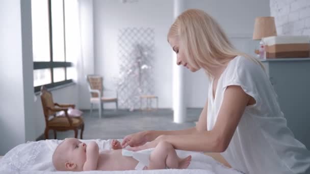 Cuidado de niños, madre joven cambia el pañal a su niña recién nacida en el cambiador de mesa en casa y luego toma al bebé en sus brazos y besos — Vídeos de Stock