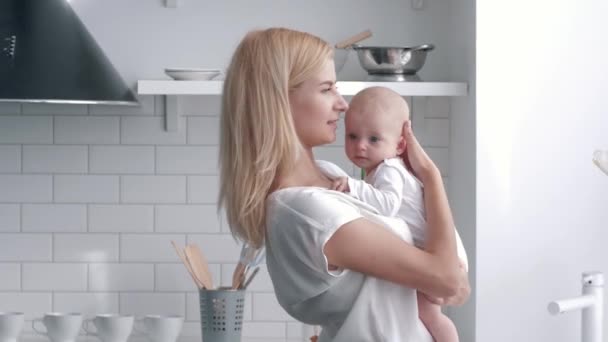 Kärleksfull mamma håller på händer nyfödda bebis flicka, porträtt av ung kvinna försiktigt kramar och kysser hennes barn i köket — Stockvideo
