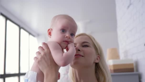 Mère embrasse doucement un nouveau-né, portrait d'une jeune femme heureuse tenant une petite fille et regardant la caméra — Video