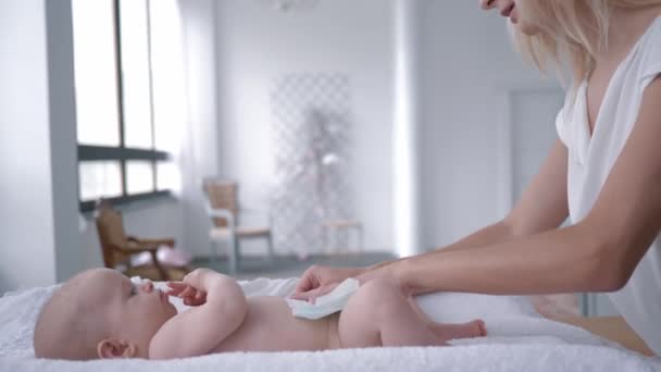 Rodičovství, pečlivá mladá matka mění plenku své novorozené holčičky při změně stolu doma zblízka — Stock video