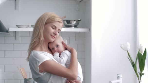 Retrato de madre joven sostiene en las manos bebé recién nacido en la cocina, padre cariñoso abrazos suavemente y besar a su hijo — Vídeo de stock