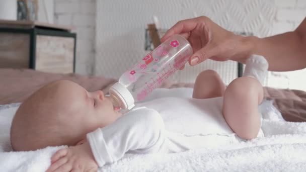 Thirsty newborn drinks water from a bottle that mother holds in her hands, little baby girl is lying on bed at home — Stock Video