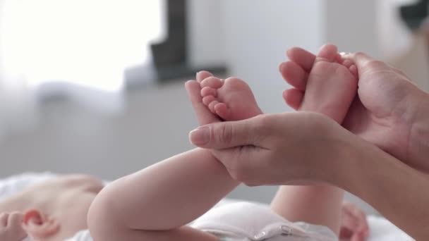 Kleine pasgeboren baby voeten in zorgzame handen van moeder close-up, kind meisje is actief bewegen liggend op veranderende tafel — Stockvideo