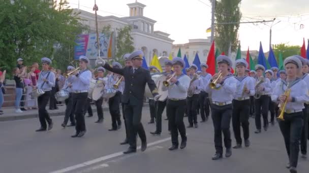 Sfilata di marinai, giovani uomini vestiti in uniforme suonano strumenti musicali e portano in mano bandiere di diversi colori camminando per una strada affollata — Video Stock