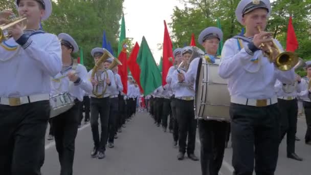 Моряки Академии морской пехоты в форме играют на музыкальных инструментах во время марша и несут красочные флаги на параде на улице — стоковое видео
