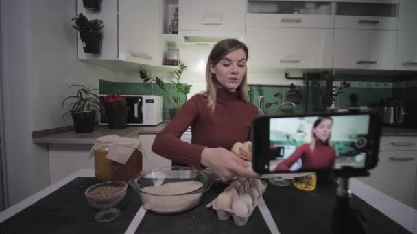 Krásná hospodyňka-blogger píše recept jídlo na smartphone pro předplatitele na sociálních sítích během živého vysílání ukazuje potřebné produkty na kameru, pak pije sklenku vína — Stock video