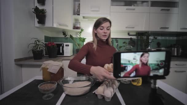 Hermosa ama de casa-blogger escribe comida de la receta en el teléfono inteligente para los suscriptores en las redes sociales durante la transmisión en vivo muestra los productos necesarios para la cámara, a continuación, bebe una copa de vino — Vídeo de stock