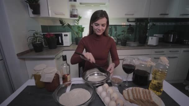 Ama de casa alegre, joven hermosa mujer divertida en la cocina se sienta a la mesa con productos para cocinar y beber vino de vidrio — Vídeo de stock