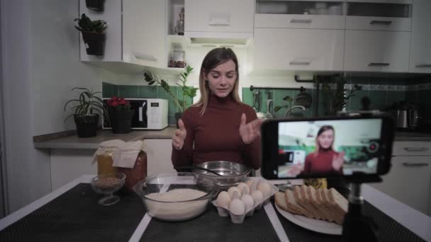 Módní blogger, roztomilý hospodyňka píše recepty na její blog na sociální síti do svého telefonu a ukazuje produkty na kameře — Stock video