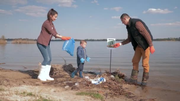 Doğa ekolojisi, küçük oğlu olan aile gönüllüleri kirli nehir kıyısındaki plastik ve polietilen çöpleri temizliyor. — Stok video