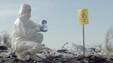 Biyolojik tehlike, koruyucu giysiler içinde tehlikeli madde kimyageri test tüpünden zehirli atık numunesi alıyor. Arazi dolgusunu biyolojik işaretle incelemek için.