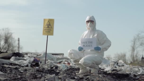 Contaminación del medio ambiente, el hombre de materiales peligrosos en uniforme muestra signo salvar el planeta en el vertedero con peligro biológico puntero — Vídeos de Stock