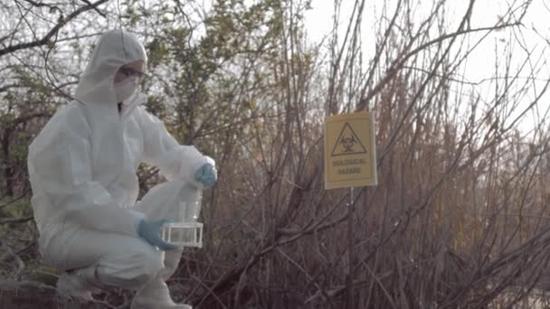 Umweltverschmutzungsproblem in der Natur, Gefahrenmatte in Schutzanzügen, die infizierte Wasserproben in Reagenzgläsern zur Untersuchung in kontaminiertem Loch mit Zeigezeichen bi entnimmt — Stockvideo