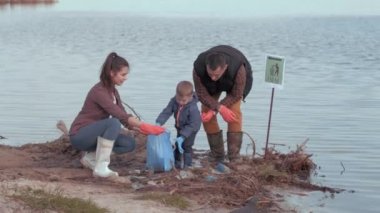 Ekolojik felaket, çocuk sahibi kadın ve erkek gönüllüler nehir kenarındaki plajda plastik ve polietilen çöpleri topluyorlar.