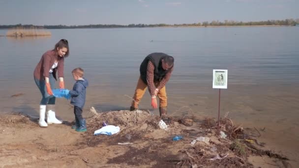 Milieubescherming, jongen helpt familie vrijwilliger activisten opruimen vervuild rivierstrand van plastic afval en verzameld in vuilniszak redden van ecologie natuur — Stockvideo