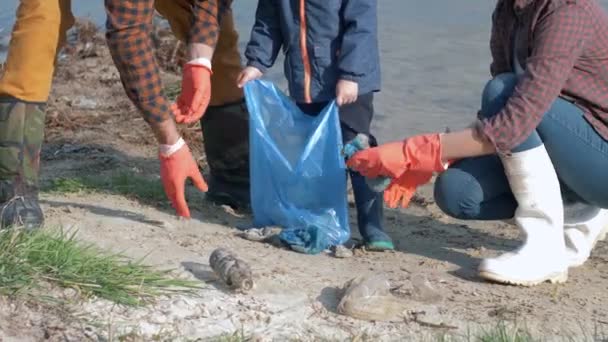 Rädda planeten från plast, unga familj volontärer med barn i gummihandskar samlar skräp i sopsäck medan rengöring smutsig vall — Stockvideo