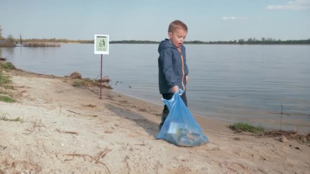 Detener la contaminación, lindo chico tira pesada bolsa de basura en señalando signo en la playa del río después de limpiar la basura de plástico y residuos domésticos — Vídeos de Stock