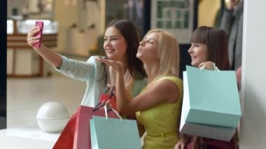 Kadın alışverişi, neşeli kız arkadaşlar, satış sezonunda ellerinde paketler ve kara Cuma indirimleriyle alışveriş yaparken cep telefonuyla fotoğraf çekiyorlar.