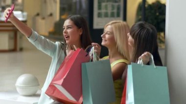 Mutlu alışverişler, şirket müşterisi kadınlar, satış sezonunda ellerinde paketler ve indirimlerle alışveriş yaparken telefonla selfie çekiyorlar.