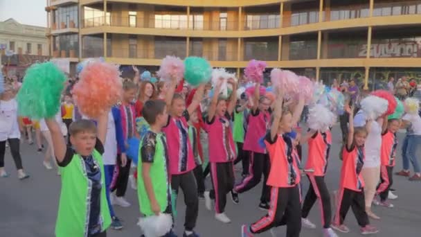 Толпа подростков в ярких костюмах, размахивающих помпонами на руках во время летнего фестиваля на городской улице в праздник — стоковое видео