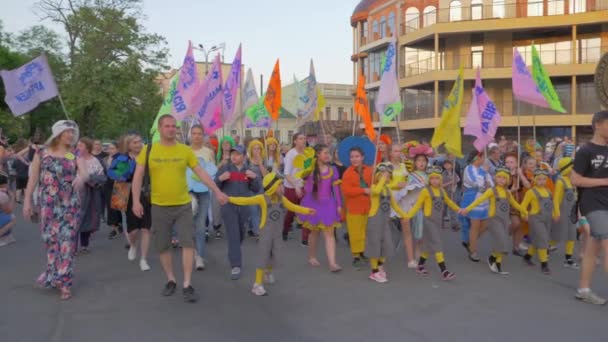 Folla felice di persone di diverse età in costumi luminosi con bandiere colorate a piedi lungo la strada della città durante il festival in estate — Video Stock