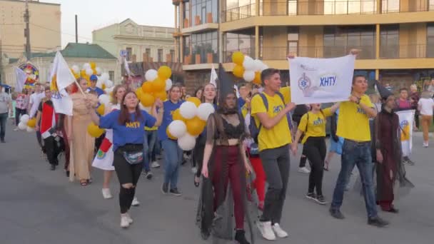 Городские традиции, толпа молодежи в разных костюмах с воздушными шарами ходить по улице города и кричать песнопения на открытом воздухе — стоковое видео