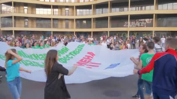 Menge junger Leute schwenkt große Leinwand bei Straßenparade in der Stadt — Stockvideo