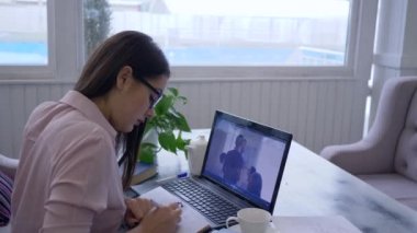 Uzaktan öğrenme, akıllı kız gözlüklü geçişler kişisel gelişim için çevrimiçi video eğitimi dizüstü bilgisayar kullanıyor ve not defterine notlar yazıyor.