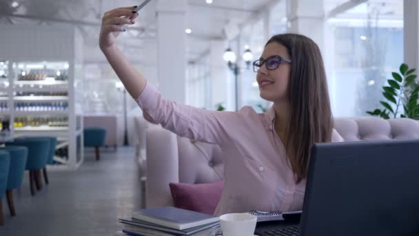 Hermosa chica propietaria del restaurante hace foto selfie en el teléfono móvil durante el trabajo en el ordenador portátil y toma notas en el cuaderno — Vídeo de stock