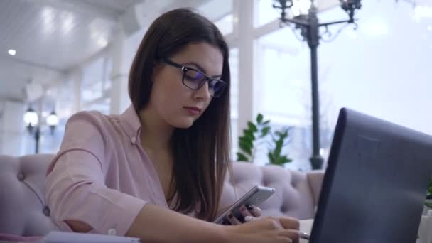 Online διάλεξη, φοιτήτρια γυναίκα συνδυάζει την εργασία και τη μελέτη χρησιμοποιώντας σύγχρονη τεχνολογία υπολογιστών με smartphone και βιβλία κρατώντας σημειώσεις στο σημειωματάριο — Αρχείο Βίντεο