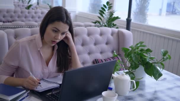 Сверхурочная работа, уставшая деловая женщина использует ноутбук для дистанционной работы с бизнес-планированием и делает заметки — стоковое видео