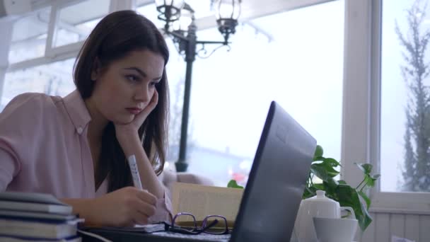 Νυσταγμένη κουρασμένη μαθήτρια χρησιμοποιεί σύγχρονη τεχνολογία υπολογιστών για να προετοιμαστεί για τις εξετάσεις από το online μάθημα κατά τη διάρκεια της εξ αποστάσεως εκπαίδευσης και σημειώνει — Αρχείο Βίντεο