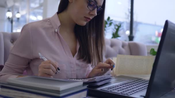 Femme d'affaires réussie dans les lunettes fonctionne avec ordinateur portable et prend des notes dans les idées d'affaires de planification de carnet — Video