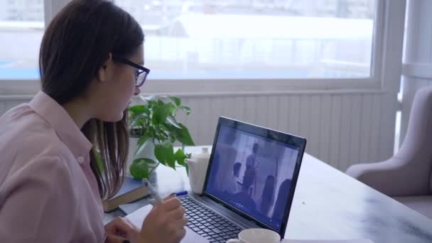 Lição on-line, mulheres estudante em óculos está aprendendo para o auto-desenvolvimento usa tecnologia moderna em treinamento e faz anotações no notebook — Vídeo de Stock
