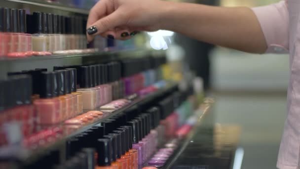 Comprador Chica elige esmalte de uñas para manicura y pedicura de gran número de botellas de esmalte de uñas en escaparate de la tienda — Vídeo de stock