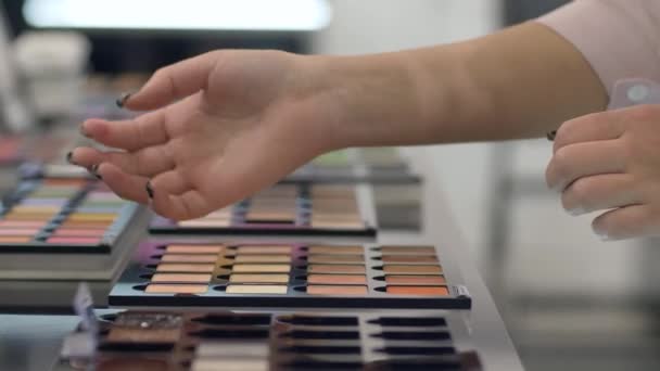 Hand van de klant vrouwelijke kiest decoratieve cosmetica uit palet van verschillende kleuren voor modieuze make-up en het testen van oogschaduw op arm in de supermarkt — Stockvideo