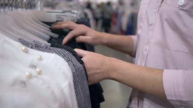 Satış indirimleri sırasında mağazadaki askılara yeni moda kıyafetler giydirmeyi düşünen müşterilerin kolları.