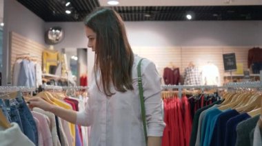 Güzel alışveriş delisi kız yeni şık kıyafetler seçiyor ve indirimler sırasında moda mağazasında aynanın karşısına geçmeye çalışıyor.