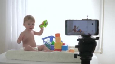 Blog yazarlığı, mutlu, gülümseyen erkek bebek oyuncaklarla oynarken ve el çırparken sosyal ağlardaki takipçilere canlı olarak akıllı telefondan canlı yayın yapıyor.